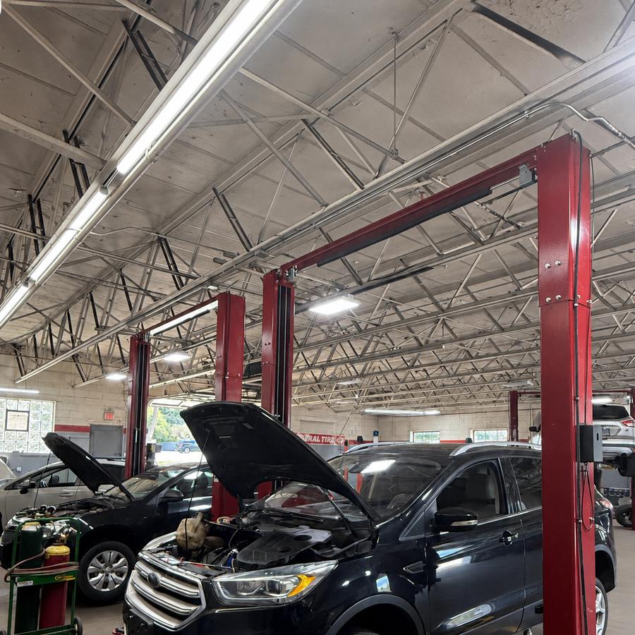 Two vehicles with hoods open on lifts in a bright service bay