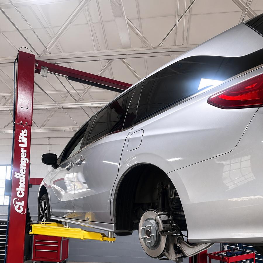 Silver minivan raised on a two post lift with the brake rotor and suspension exposed