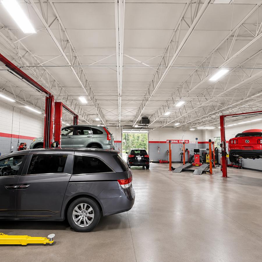 Wide view of a clean service floor with several vehicles on red two post lifts